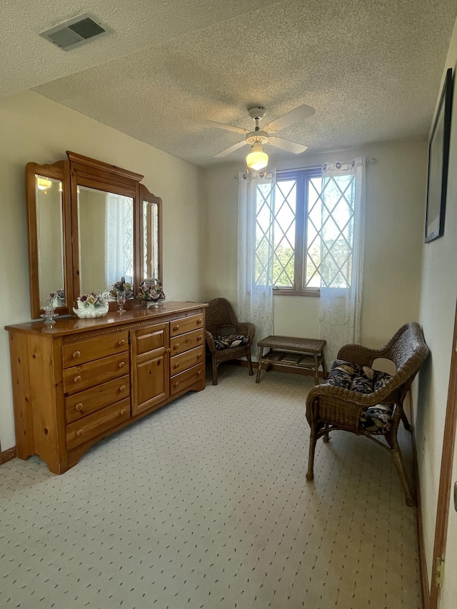 sitting room featuring light carpet, a ceiling fan, visible vents, and a textured ceiling