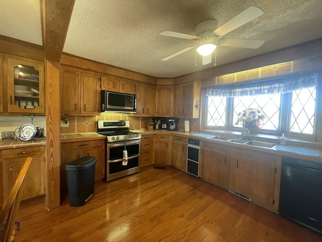 kitchen with decorative backsplash, brown cabinetry, a sink, wood finished floors, and black appliances