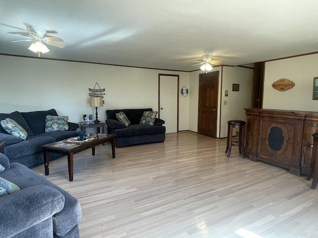 living room with ceiling fan, light wood finished floors, a textured ceiling, and ornamental molding