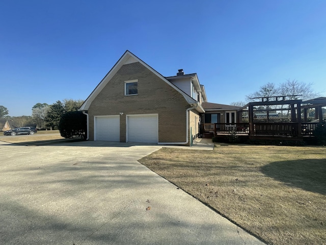 view of property exterior featuring a lawn, concrete driveway, an attached garage, a deck, and brick siding