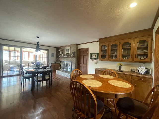 dining room with a brick fireplace, ornamental molding, dark wood finished floors, and a textured ceiling