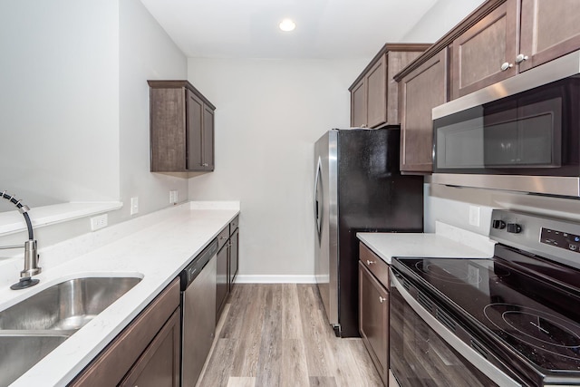 kitchen with baseboards, a sink, stainless steel appliances, dark brown cabinets, and light wood-type flooring