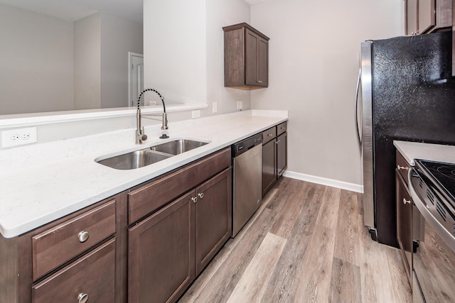 kitchen featuring light wood finished floors, stainless steel appliances, light countertops, and a sink