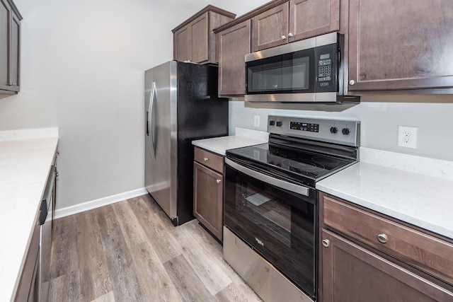 kitchen with baseboards, dark brown cabinetry, light countertops, light wood-style floors, and stainless steel appliances