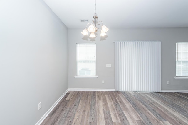 empty room featuring visible vents, baseboards, a notable chandelier, and wood finished floors