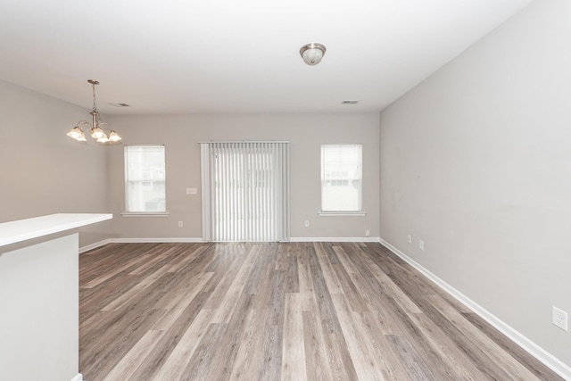 unfurnished room with light wood-style flooring, a notable chandelier, baseboards, and a wealth of natural light