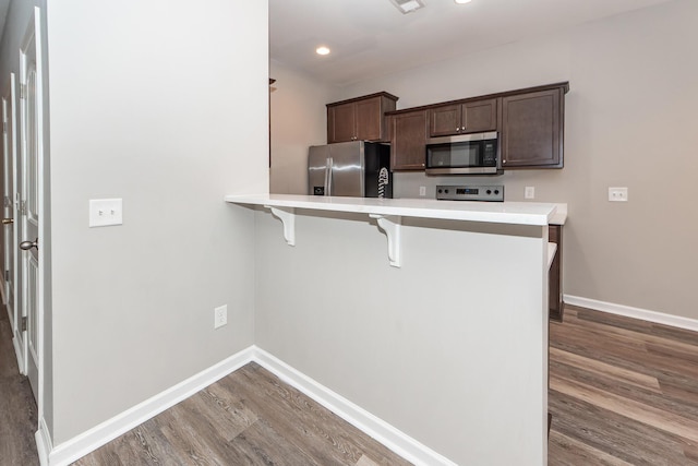 kitchen featuring a breakfast bar area, dark brown cabinets, baseboards, and appliances with stainless steel finishes