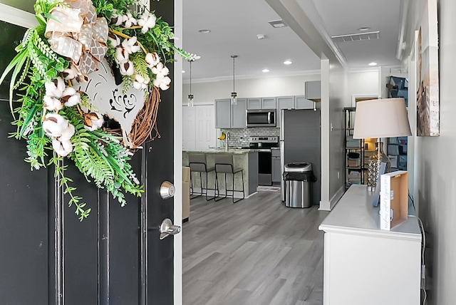 kitchen featuring hardwood / wood-style flooring, gray cabinetry, stainless steel appliances, ornamental molding, and decorative backsplash