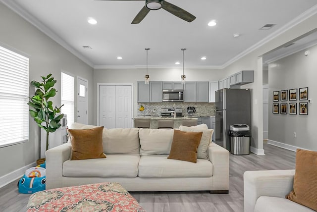 living room with ornamental molding, ceiling fan, and light wood-type flooring