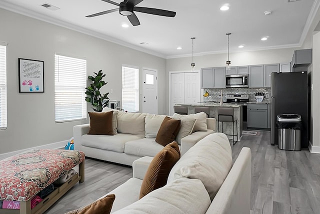 living room with ornamental molding, wood-type flooring, sink, and ceiling fan