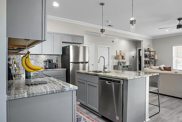 kitchen with gray cabinetry, crown molding, decorative light fixtures, a center island with sink, and appliances with stainless steel finishes