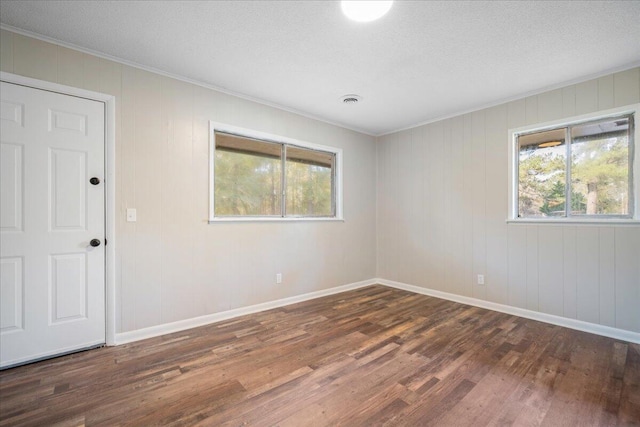 unfurnished room featuring wooden walls, dark hardwood / wood-style flooring, a textured ceiling, and ornamental molding