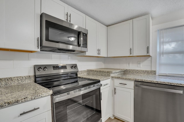 kitchen featuring a textured ceiling, light stone counters, white cabinetry, and stainless steel appliances