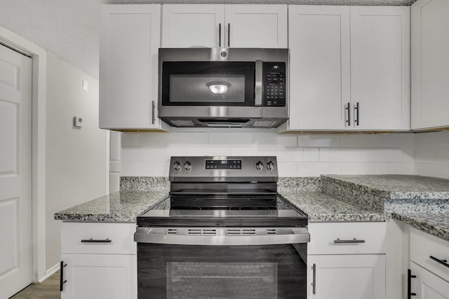 kitchen featuring tasteful backsplash, light stone countertops, white cabinets, and appliances with stainless steel finishes