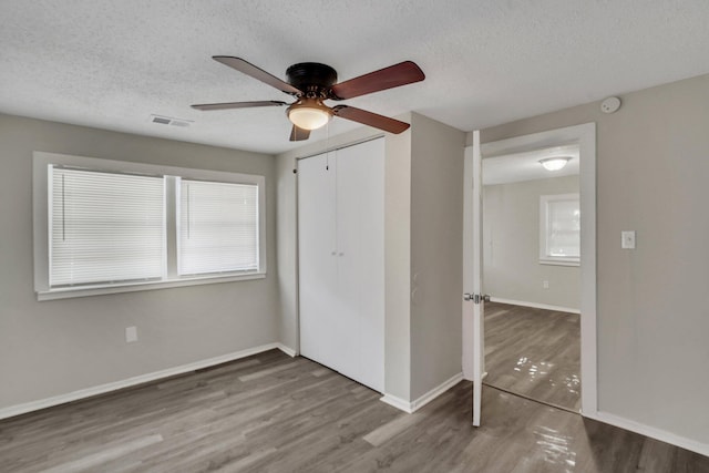 unfurnished bedroom featuring multiple windows, wood-type flooring, and ceiling fan