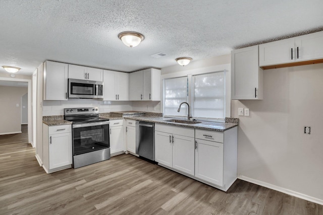 kitchen featuring stone counters, sink, stainless steel appliances, white cabinets, and light wood-type flooring