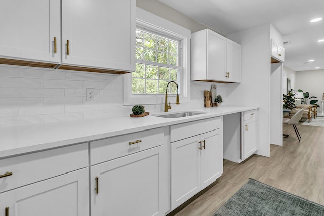 kitchen featuring white cabinets, tasteful backsplash, light wood-type flooring, and sink