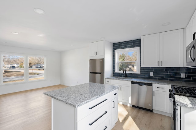 kitchen with a kitchen island, white cabinetry, backsplash, stainless steel appliances, and light wood-type flooring