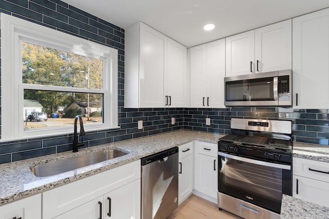 kitchen featuring light stone counters, a sink, white cabinetry, appliances with stainless steel finishes, and decorative backsplash