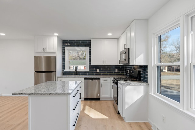 kitchen with stainless steel appliances, light stone countertops, a center island, and white cabinets