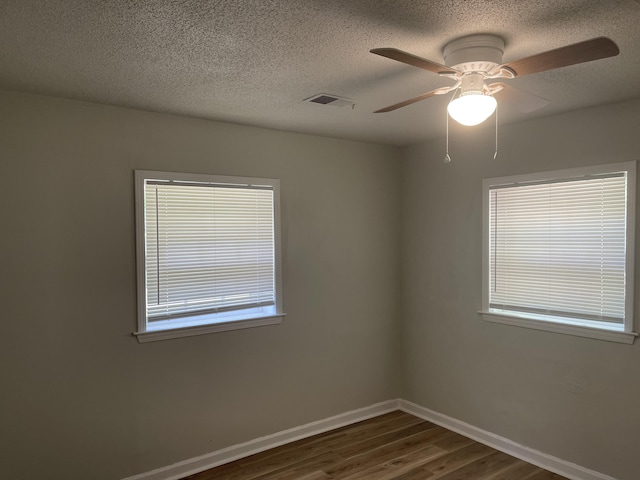 unfurnished room featuring baseboards, a textured ceiling, a ceiling fan, dark wood-type flooring, and visible vents