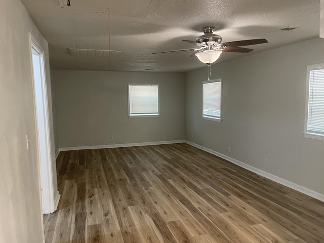 empty room featuring plenty of natural light, a textured ceiling, attic access, visible vents, and wood finished floors