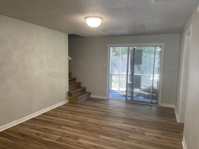 empty room with dark wood-type flooring, baseboards, stairway, and a textured ceiling