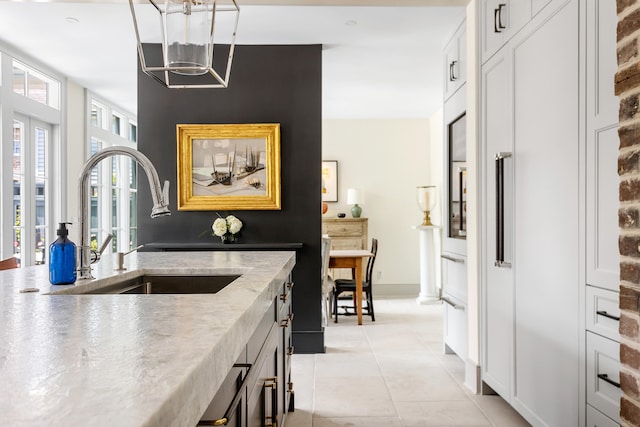 kitchen featuring a sink, white cabinetry, light tile patterned floors, baseboards, and light stone countertops