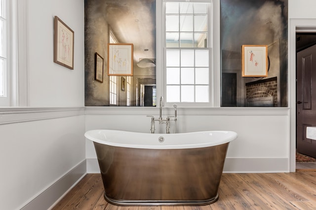 full bathroom with a freestanding tub, baseboards, and wood finished floors