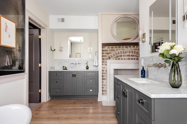 bathroom with visible vents, two vanities, a sink, backsplash, and wood finished floors