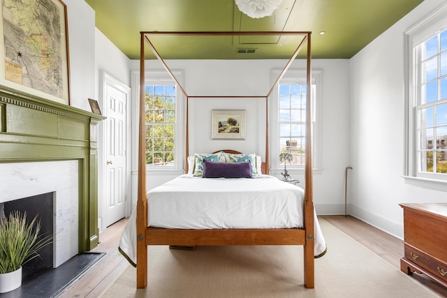 bedroom with a high end fireplace, visible vents, multiple windows, and wood finished floors