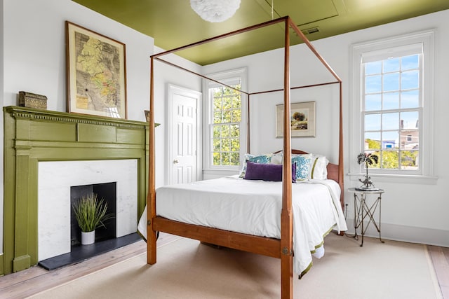 bedroom with visible vents, a fireplace, baseboards, and wood finished floors