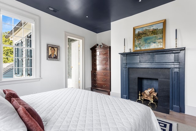 bedroom featuring a fireplace, ensuite bath, wood finished floors, and visible vents