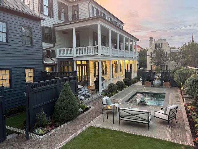 back of house at dusk featuring a fenced backyard, a balcony, a standing seam roof, and a patio