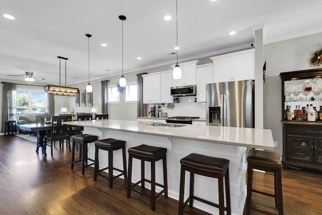 kitchen with pendant lighting, sink, appliances with stainless steel finishes, white cabinetry, and a large island with sink