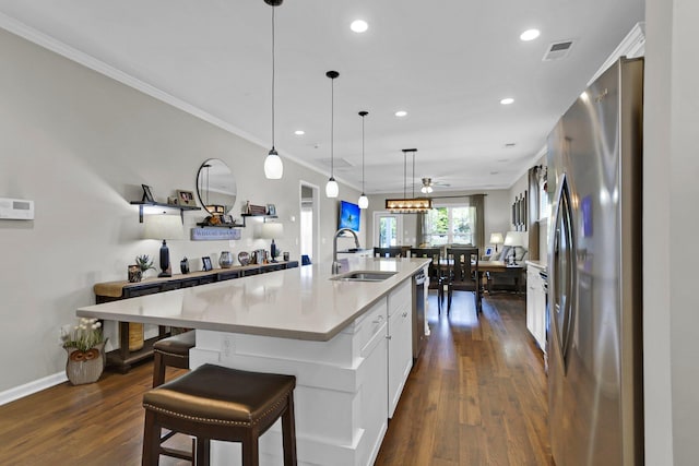 kitchen with decorative light fixtures, sink, white cabinets, a large island with sink, and stainless steel appliances