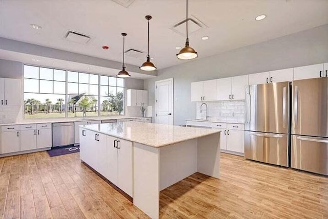 kitchen with hanging light fixtures, a kitchen island, white cabinets, stainless steel appliances, and backsplash