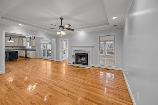 unfurnished living room featuring ceiling fan, a fireplace, ornamental molding, light hardwood / wood-style floors, and a raised ceiling