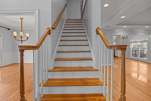 stairs featuring crown molding, wood-type flooring, and a notable chandelier