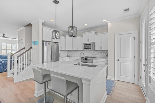 kitchen with sink, appliances with stainless steel finishes, a kitchen island with sink, light stone counters, and white cabinets