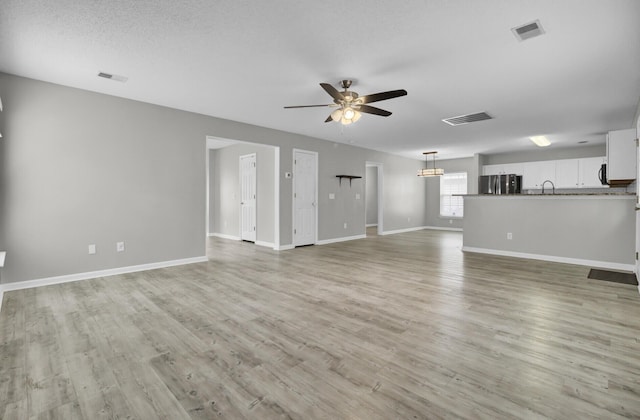 unfurnished living room with ceiling fan with notable chandelier, a textured ceiling, and light wood-type flooring