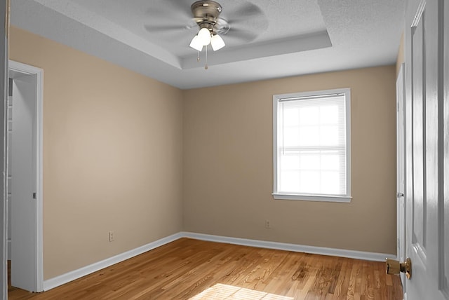 unfurnished room featuring ceiling fan, a tray ceiling, a textured ceiling, and light wood-type flooring