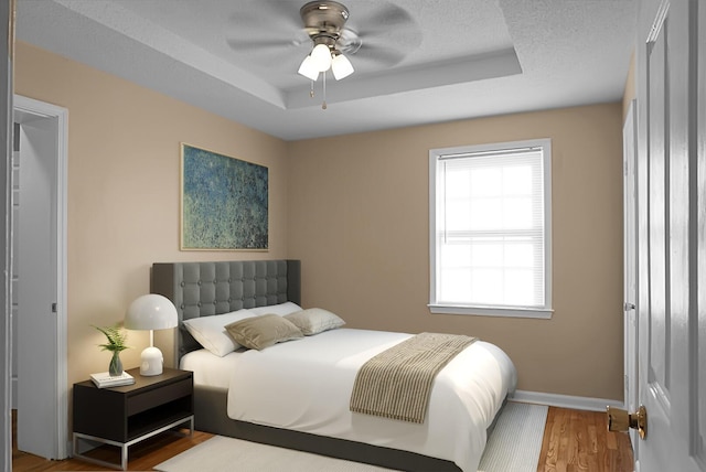 bedroom featuring a raised ceiling, wood-type flooring, ceiling fan, and a textured ceiling