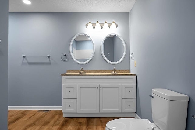 bathroom with wood-type flooring, toilet, a textured ceiling, and vanity