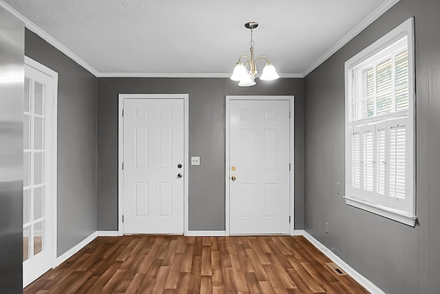 foyer entrance with dark hardwood / wood-style flooring, a textured ceiling, ornamental molding, and a chandelier