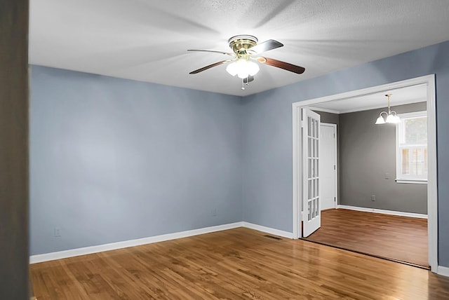 spare room featuring wood-type flooring, ceiling fan with notable chandelier, and a textured ceiling