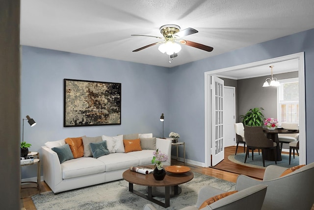 living room featuring hardwood / wood-style floors, ceiling fan with notable chandelier, and a textured ceiling