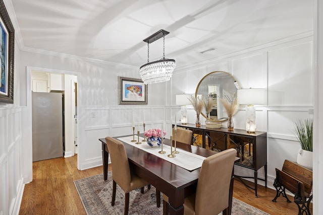 dining room with crown molding, wood-type flooring, and an inviting chandelier