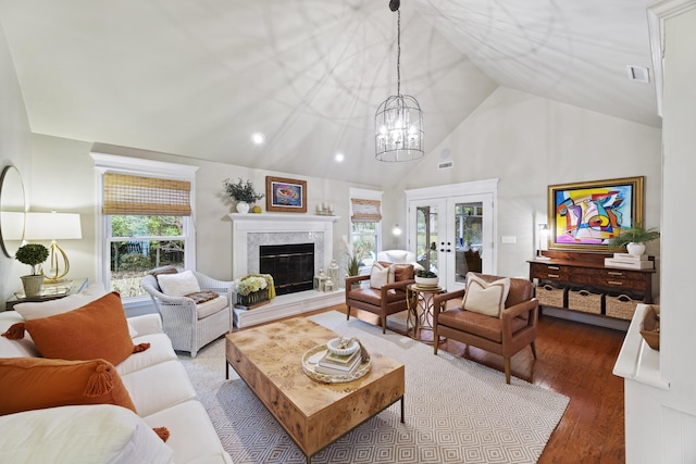 living room with high vaulted ceiling, french doors, a high end fireplace, an inviting chandelier, and wood-type flooring