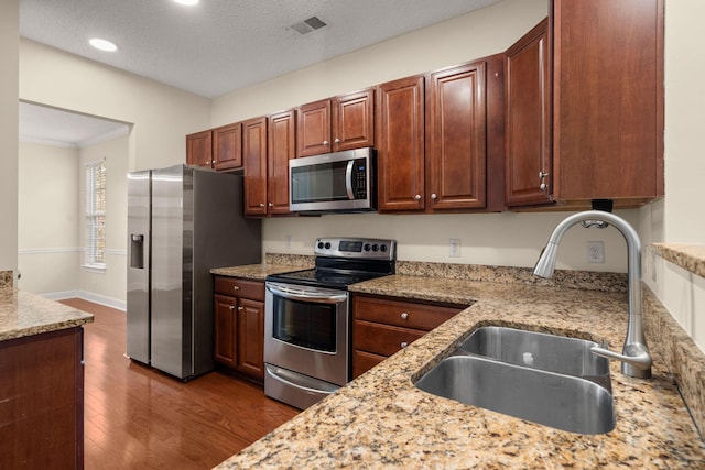 kitchen featuring sink, light stone countertops, a textured ceiling, dark hardwood / wood-style flooring, and stainless steel appliances